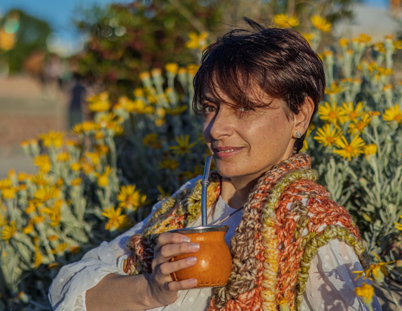 The Art of Drawing Readers In: Your attractive post title goes here Woman with handcrafted scarf sipping yerba mate outdoors in Montevideo. Vibrant yellow flowers in full bloom.